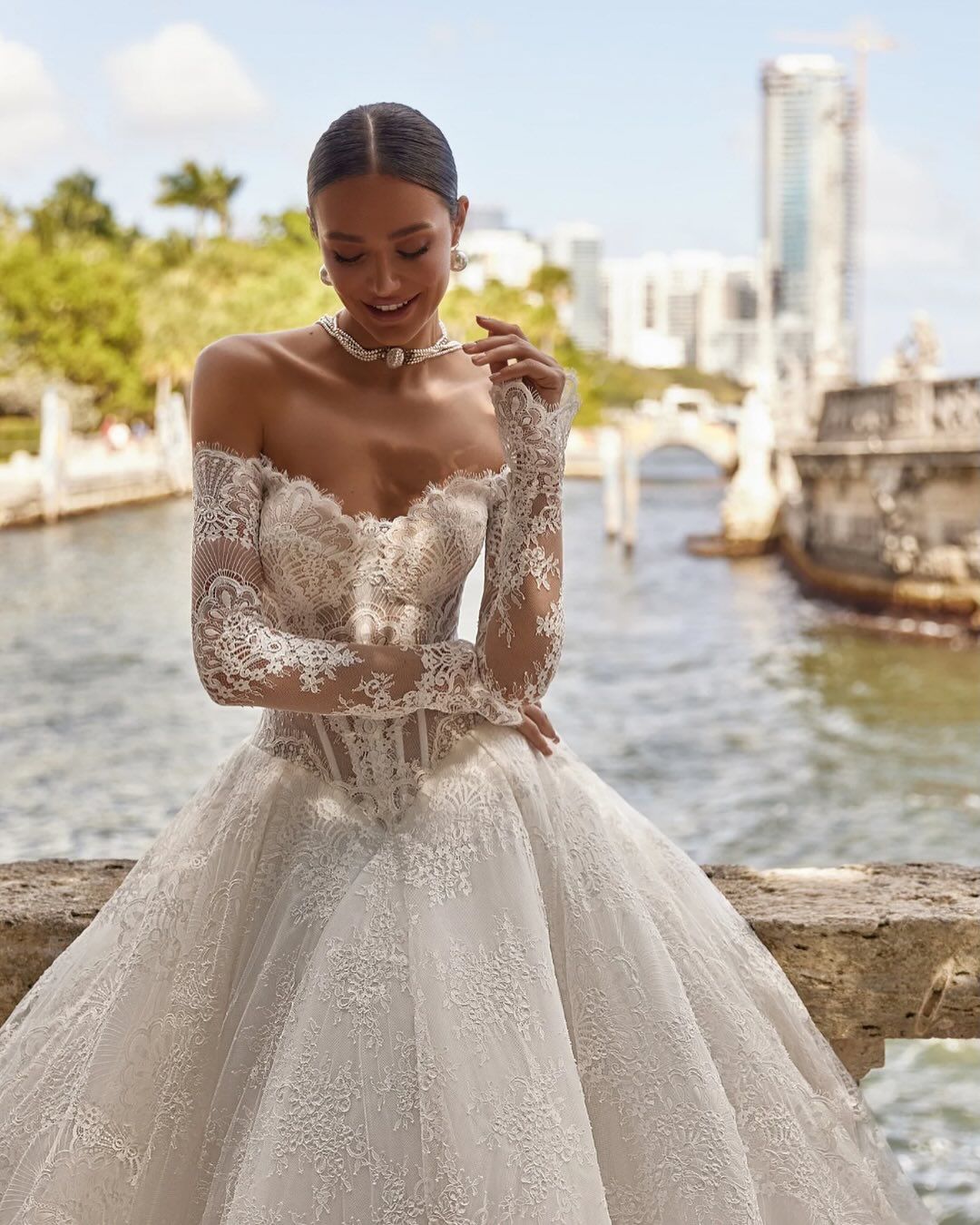 Bride in a full-skirt wedding gown holding a bouquet beside the water