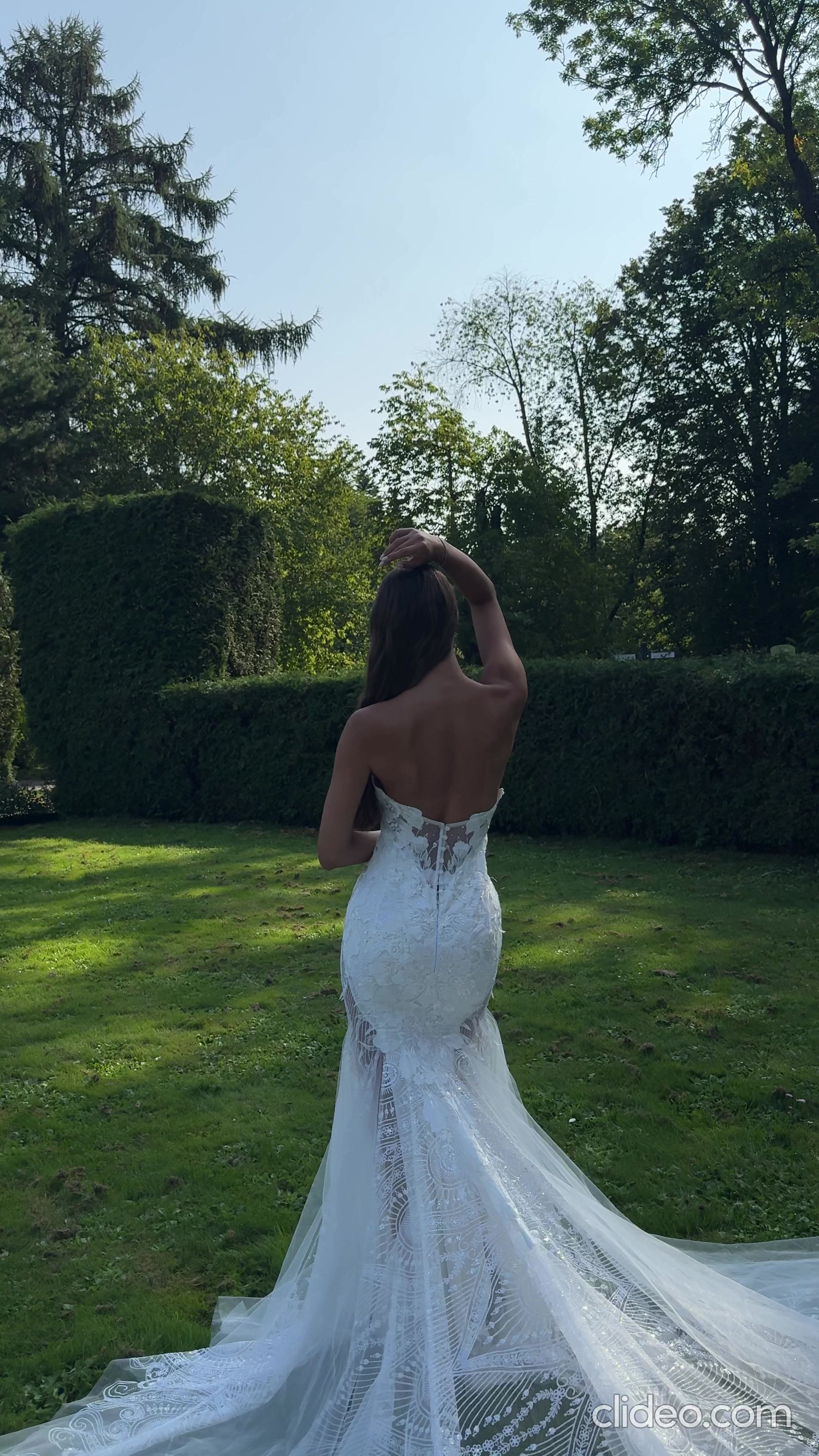 Back of a fitted lace wedding gown with a long train in a garden