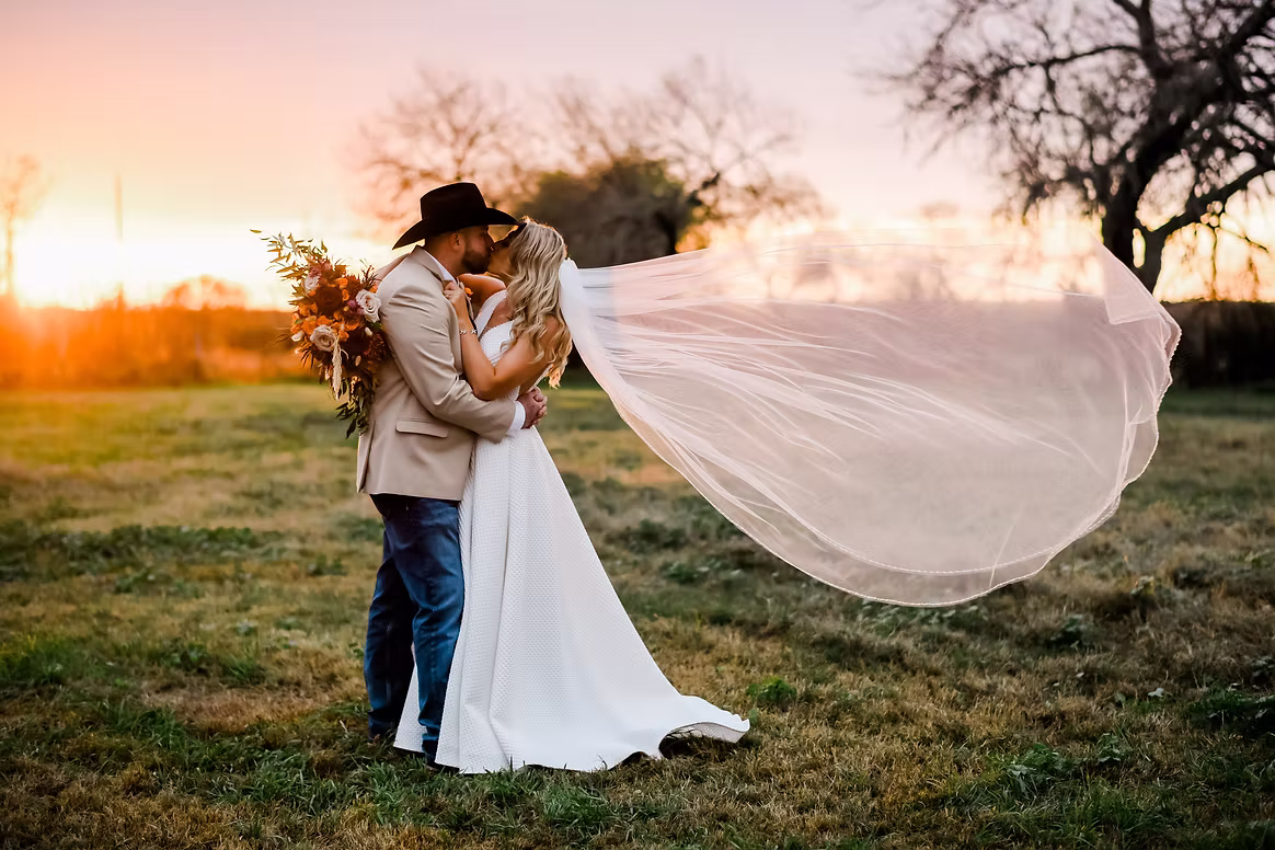 Newlyweds embracing at sunset with a veil blowing in the breeze