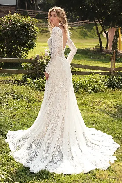 Long-sleeved lace wedding gown with a train outdoors.