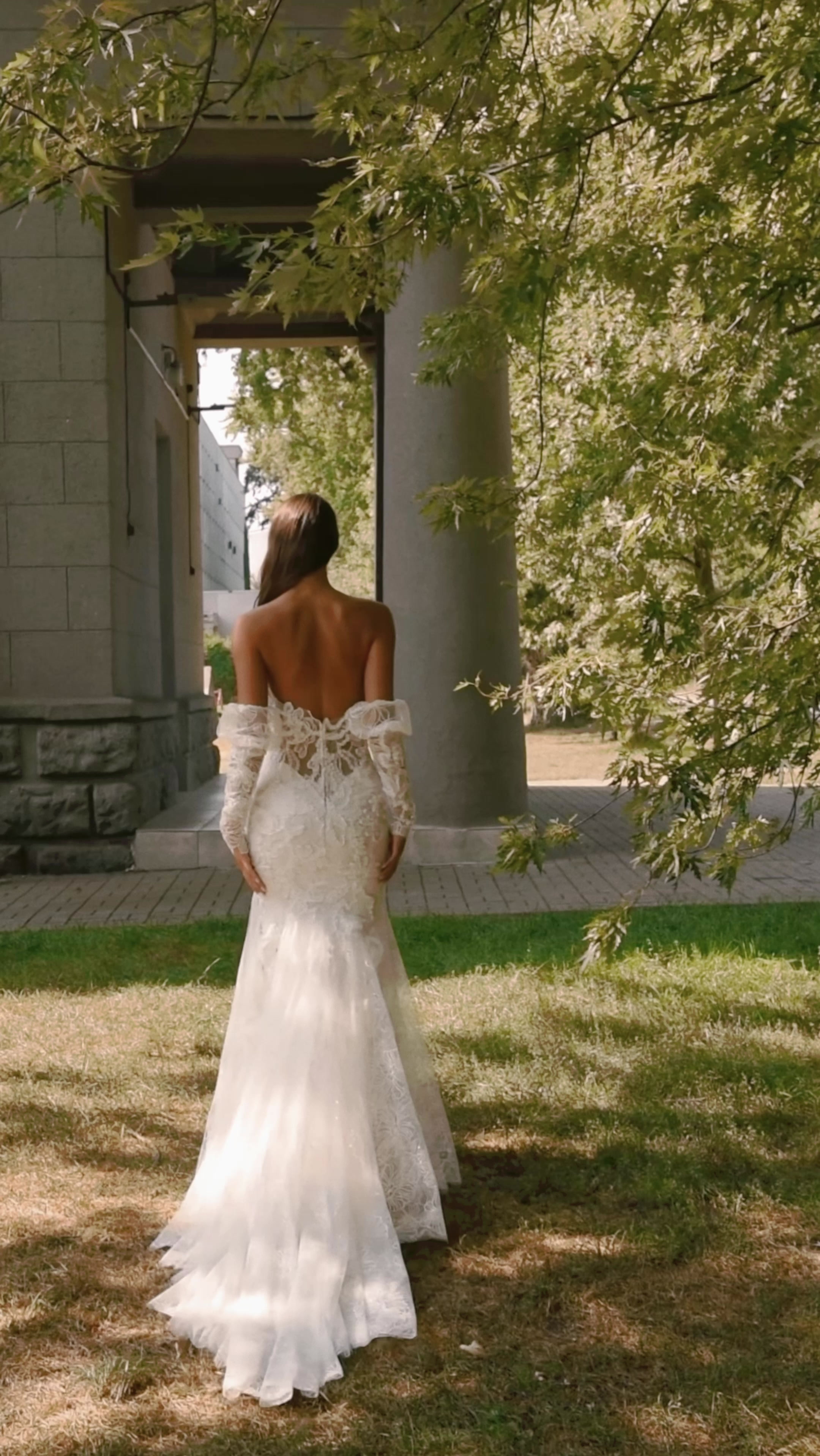 Bride in a fitted off-shoulder lace gown beside a garden pavilion