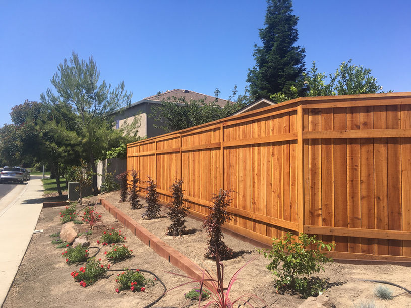 Stained redwood fence installation by Fence Lifts beside front yard driveway