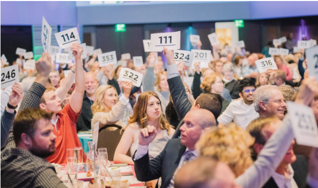 room full of people holding up white pieces of paper with numbers on them