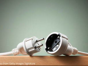 a simple, close-up photo of a white electrical plug and its matching socket lying disconnected on a wooden tabletop