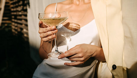 Luxurious woman wearing a white dress, holding a coupe with champagne in sun light. Concep
