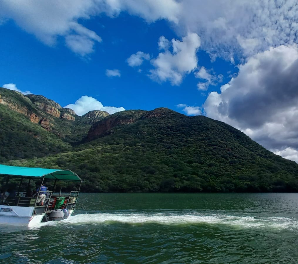 A peaceful boat cruising through the deep waters of the Blyde River Canyon with towering cliffs.