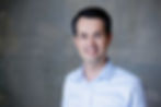 Sebastian Stiewe steht vor einer grauen Wand und schaut lächelnd ins Bild.
