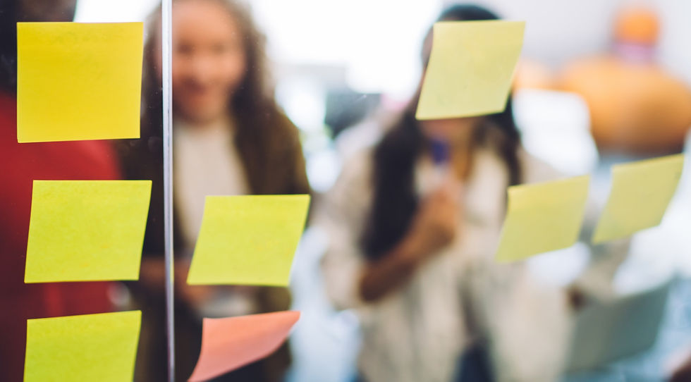 Glass with yellow stickers and coworkers gathering in office standing behind glass wall and planning