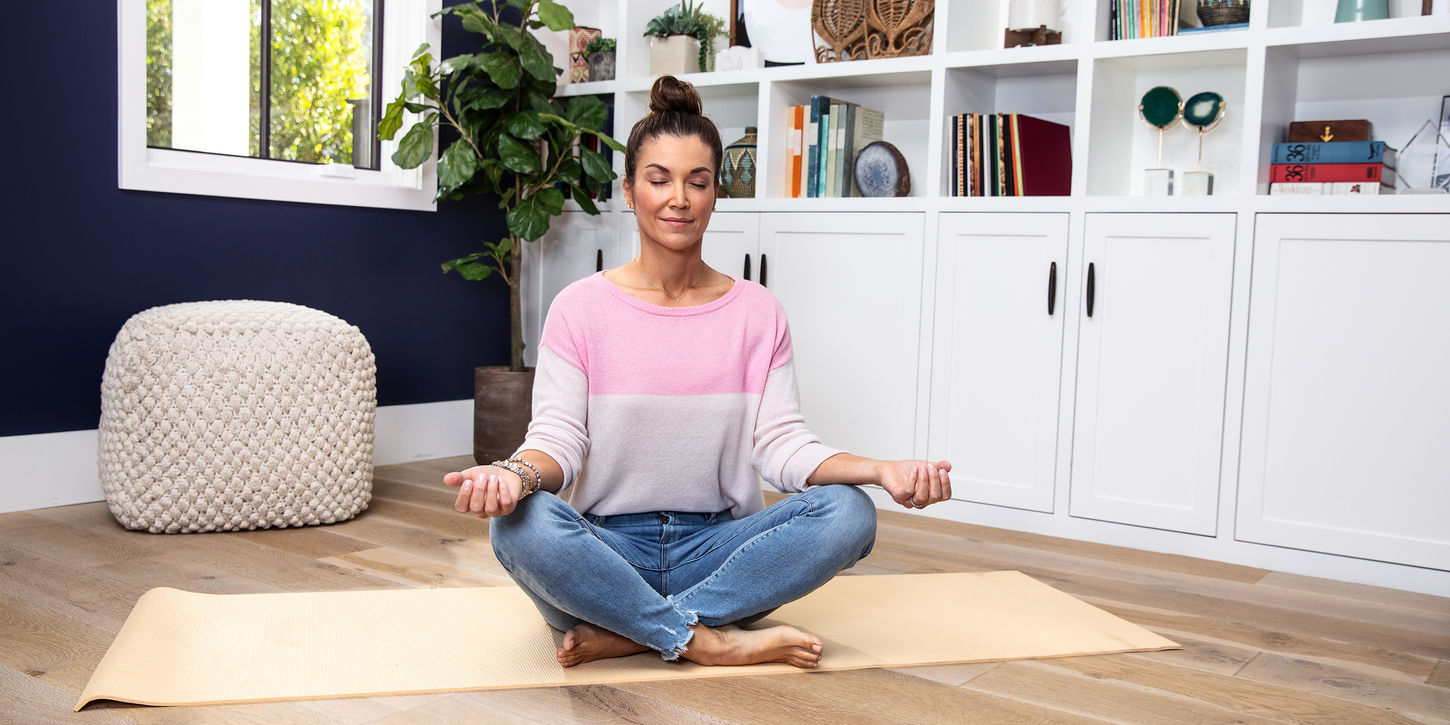 A woman sits meditating in her home.