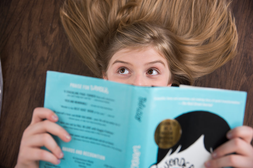 Dark blonde girl with brown eyes reading Wonder book while laying on floor.