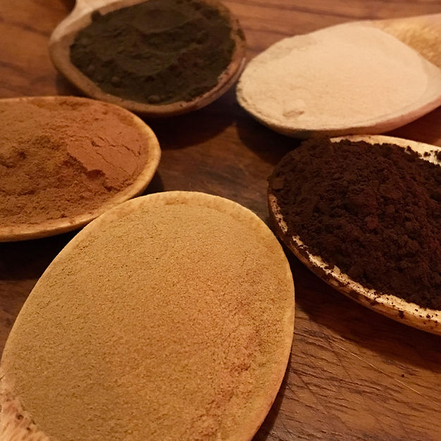 wooden spoons arranged in a circle, each displaying different powdered herbal extracts of varying colors