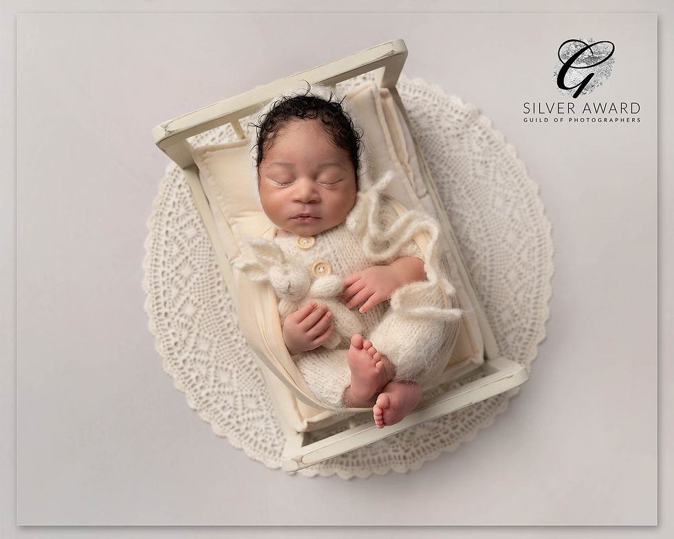 Newborn image of a baby on a tiny bed holding a bunny in cream colours complimented by a lace layer under the bed.