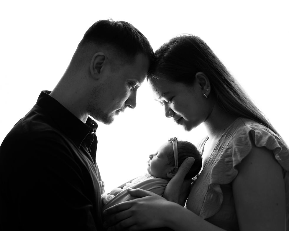 Backlit family portrait of mum and dad holding newborn baby between them