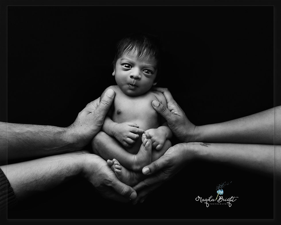 Newborn being held in parents hands, black and white image.