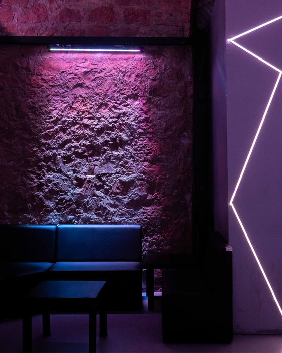 Interno bar con muro di pietra, neon rosa e divanetti neri