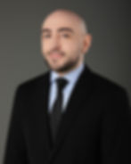 Rati Romanadze at Aspecture Global hospitality consulting in Vietnam. In a black suit and tie, a light blue shirt, smiling against a dark gray background. Professional and confident mood.