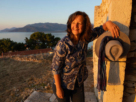 Desiree Driesenaar at a Peloponnese castle, hat in hand, sunrise lighting, looking over the Mediterranean