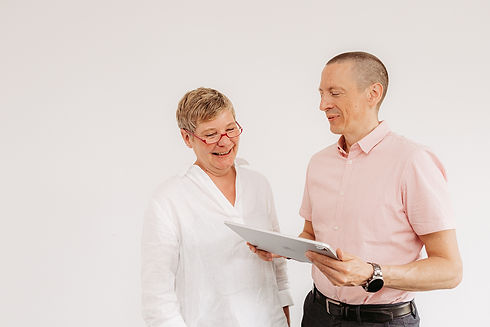 Eine Frau und ein Mann stehen beiander, der Mann hält ein Tablet in seiner Hand und zeigt es der Frau, die Frau schaut drauf und lächelt.