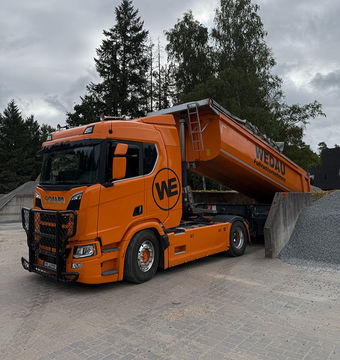 Oranger Müllwagen entlädt Schutt aus Container