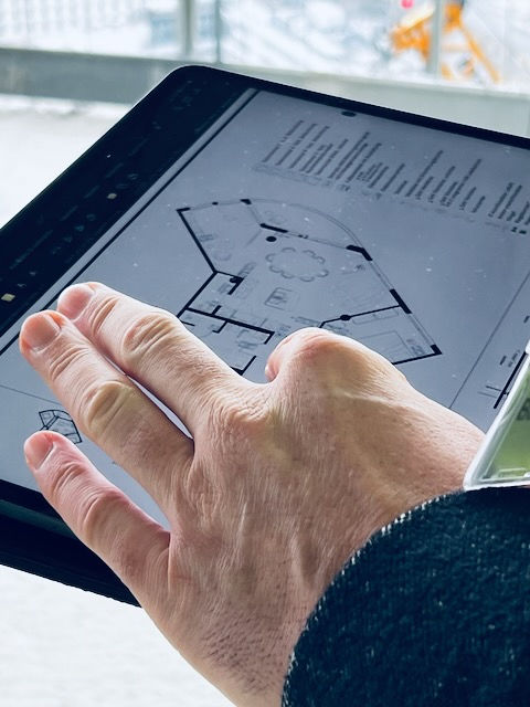 Nahaufnahme einer Hand, die auf einem Tablet einen Grundriss eines Apartments im FOUR Frankfurt betrachtet. Die Szene zeigt, wie raumstation interior design Architektur, Innenarchitektur und Interior Design bereits im Rohbau digital analysiert und präzise geplant werden, um optimale Raumkonzepte zu entwickeln.