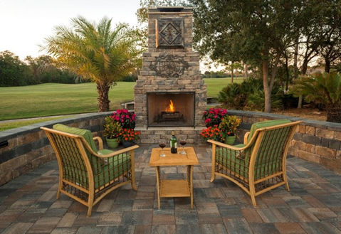 backyard patio with lit tiki torches and brick fire place with a golf course in the background