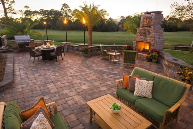 backyard patio with lit tiki torches and brick fire place with a golf course in the background