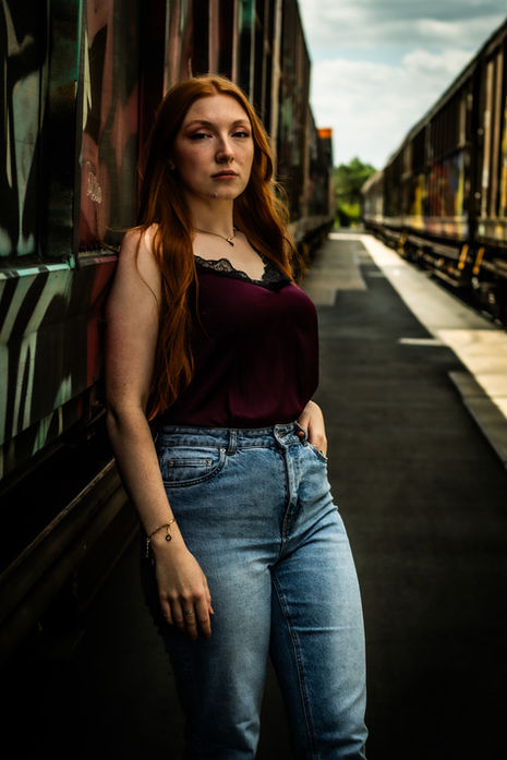 Frau in dunklem Top und Jeans steht auf einer Brücke bei einem urbanen Outdoor-Portrait.