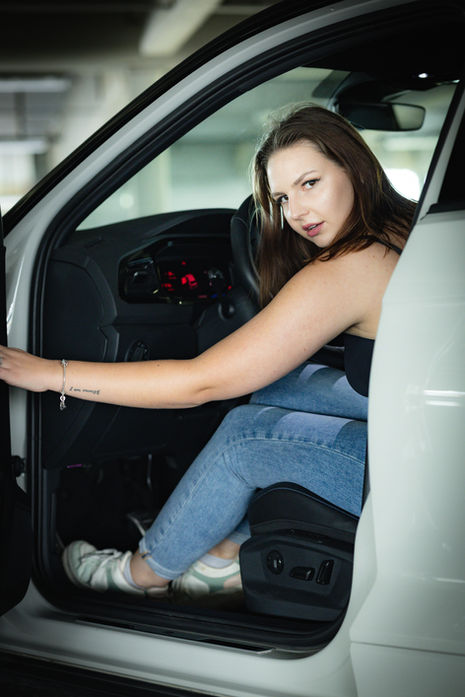 Frau sitzt im geöffneten Auto und posiert mit einer Hand am Lenkrad.