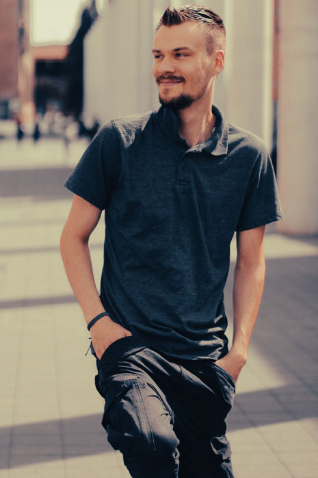 Mann in dunklem Poloshirt steht entspannt bei einem urbanen Outdoor-Shooting.