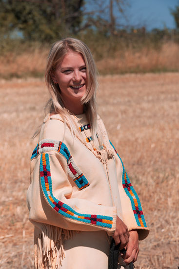 Lächelnde blonde Frau in hellem Fransen-Outfit bei einem sommerlichen Outdoor-Portrait.