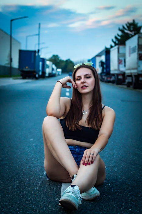Frau sitzt auf einer Straße in einem Industriegebiet bei einem urbanen Outdoor-Portrait.