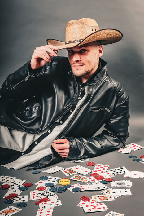 Mann mit Cowboyhut und Lederjacke posiert am Pokertisch und berührt die Hutkrempe.
