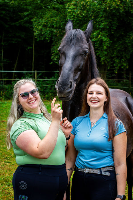 Zwei Frauen lachen gemeinsam vor einem schwarzen Pferd bei einem lockeren Pferdeshooting im Grünen.