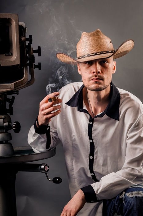 Mann mit Cowboyhut sitzt bei einem Studio-Portrait neben professioneller Kameraausrüstung.