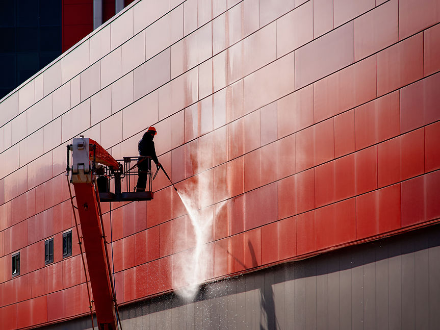Worker wearing safety harness washes wall facade at height on modern building in a crane.j