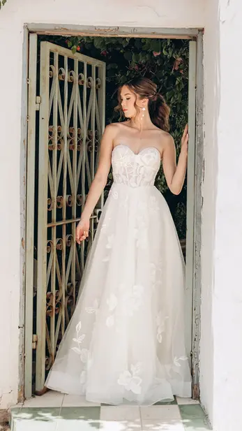 MODERN OVERSIZED LACE STRAPLESS A-LINE WEDDING DRESS WITH SWEETHEART NECKLINE

A modern lace wedding gown that exudes chic sophistication, Style 7975’s elegant A-line silhouette marries grace and glamour for an unforgettable wedding day look. The sculpted strapless bodice features a modern sweetheart neckline and sheer corset-style construction, offering a tailored effect that accentuates the natural silhouette. Large-scale floral lace adds a bold, fashion-forward element, while the basque waist and sheer back detail creates a striking transition to the frothy layered skirt, scattered in romantic oversized floral lace appliqués. Blending timeless elegance and modern glamour, this chic strapless wedding dress is ideal for the Stella York bride seeking a fresh take on classic bridal style.