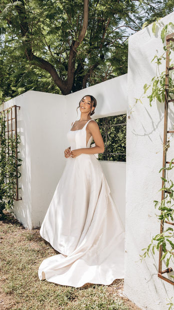 Simple Minimalist A-Line Wedding Dress with Square Neckline and Detachable Bow
Style 8031 redefines bridal elegance with a modern, minimalist approach to creating a luxe A-line wedding dress that stands the test of time. This simple wedding dress features a refined square neckline framed by modest shoulder straps, setting the tone for its contemporary chic aesthetic. The gown’s clean lines are accentuated by the vertical seams running the length of the dress, perfectly highlighting the figure and graceful A-line silhouette. A touch of elegance is added with modest side cutouts that dip to a drop waist in the back, where an oversized detachable Mikado bow makes a striking fashion statement. Crafted entirely in luxe Mikado fabric, this dress shimmers and glistens in the light, creating a unique bridal look that’s both timeless and distinct. This gown is also available in plus sizes.