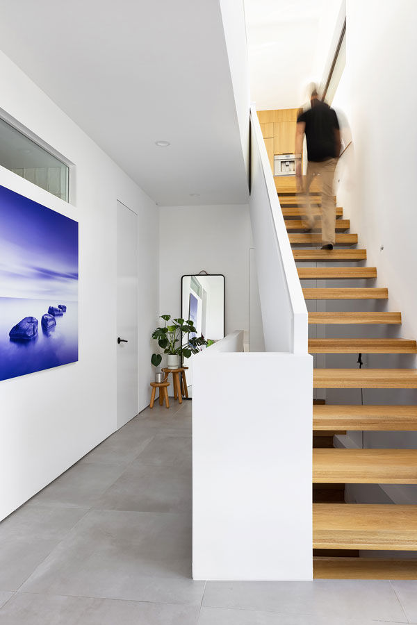 Double-height ceilings and an open-riser staircase “draw your attention away from the private rooms on the main floor and up to the living room on the second floor,” Hom says. Large-format porcelain tile flooring — used here and throughout — is easy to clean and maintain, he adds. Behind the transom window is a guest bathroom. The door at left leads to the primary suite.