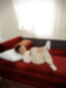 Kind liegt entspannt auf einem roten Sofa in einem hellen Zimmer.