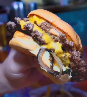 Customer holding a "Lokul Burger" from Lokul Jamul Tap and Grill with double smashed wagyu patties, melted cheese and grilled onions.