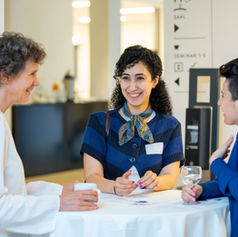 Drei Frauen stehen an einem Tisch und unterhalten sich lachend bei einer Veranstaltung. Die Szene vermittelt Networking und Freude am Austausch in einem beruflichen Kontext. 