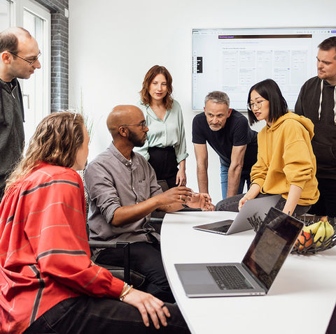 Corporate Fotografie eines diversen Teams bei einer Besprechung in einem modernen Berliner Büro. Die Mitarbeitenden diskutieren gemeinsam ein Projekt am Konferenztisch, während im Hintergrund ein digitales Board mit einem Business Model Canvas zu sehen ist.