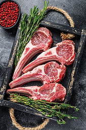 Raw lamb meat chops steaks in a wooden tray. Black background. Top view..jpg