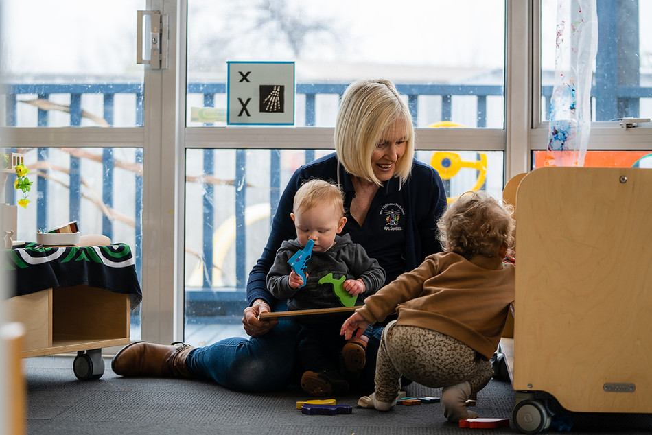 Nursery school teacher assisting with play with puzzles with two toddlers