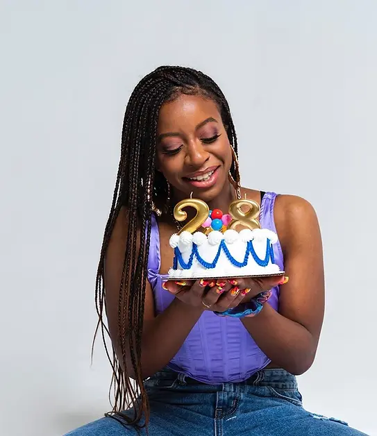 A woman holding a birthday cake with candles shaped like the number 28