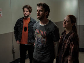 A man stands in a dim psychiatric hospital hallway with eerie shadows surrounding him.