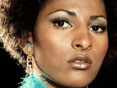 Pam Grier stands confidently in a classic film still.
