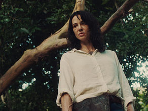 A woman stands in a decaying plantation surrounded by tense figures.