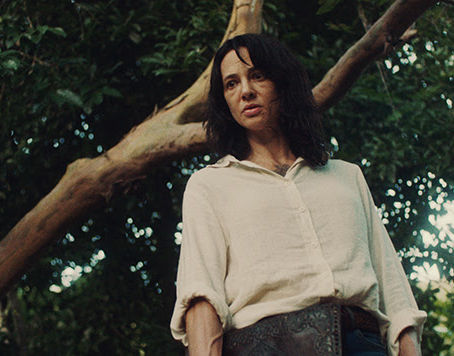 A woman stands in a decaying plantation surrounded by tense figures.