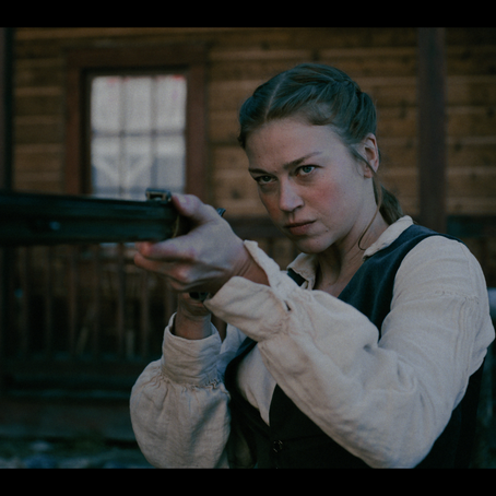 A distressed woman stands in a foggy rural town surrounded by suspicious villagers.